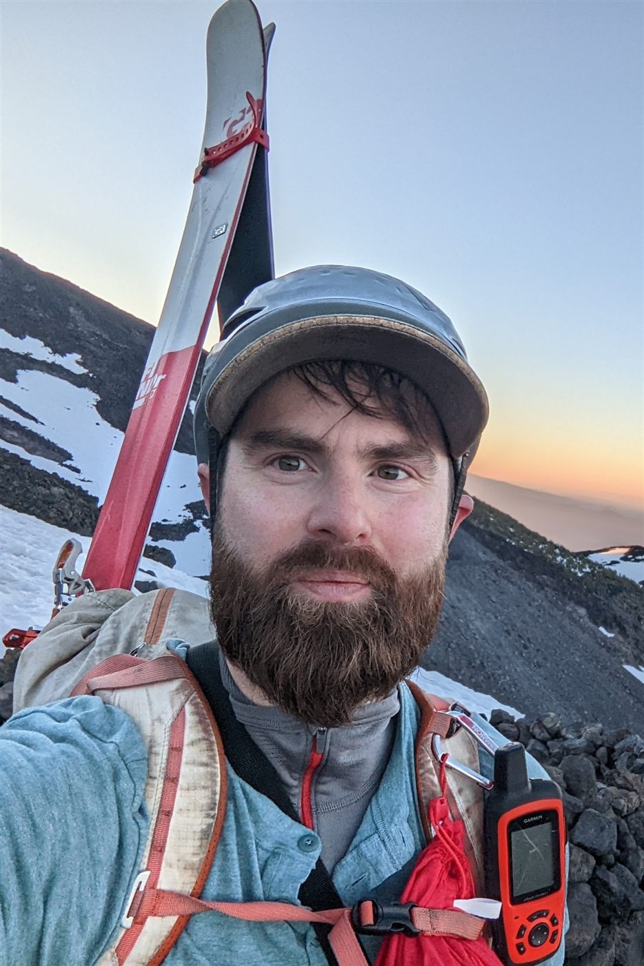 Laurence on a mountainside at sunrise, skis strapped to his pack